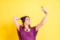 Young pretty woman takes a picture of herself with her mobile, isolated on yellow studio background Royalty Free Stock Photo