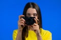 Young pretty woman takes pictures with DSLR camera over blue background in studio. Girl smiling as photographer. Royalty Free Stock Photo
