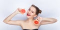 Young pretty woman trendy makeup bright red lips bun hairstyle bare shoulders act the ape with grapefruits white studio background