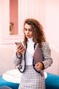 Young woman using smart phone while standing against the wall. In other hand holding laptop Royalty Free Stock Photo