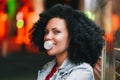 Young pretty woman with very curly afro hair inflates a bubble ball of white chewing gum at night. Trendy girl having Royalty Free Stock Photo