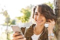 Young pretty woman walking outdoors in park in beautiful spring day using mobile phone Royalty Free Stock Photo