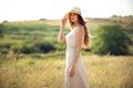 young pretty woman walks on field in summer while wearing a sunhat and midi dress. Lifestyle