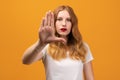 Young pretty woman showing open palm making stop gesture. Studio shot, yellow background. Human emotions concept