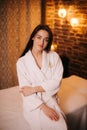 Young pretty woman in white bathrobe sitting on massage table in spa salon Royalty Free Stock Photo