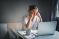 Young pretty woman in a white shirt sits at a table in front of a laptop, her eyes and head ache, workaholism, stress burnout Royalty Free Stock Photo