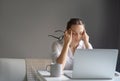 Young pretty woman in a white shirt sits at a table in front of a laptop, her eyes and head ache, workaholism, stress burnout Royalty Free Stock Photo