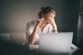 Young pretty woman in a white shirt sits at a table in front of a laptop, her eyes and head ache, workaholism, stress burnout Royalty Free Stock Photo