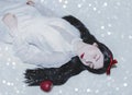 Young pretty woman with white skin and red lips is lying on the snow with red poisoned apple.Snow white princess