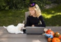 Young pretty woman in witch hat. Sits at table in garden, works at laptop