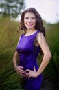 Young pretty women with long windy hair in elegant violet dresses standing on green grass Royalty Free Stock Photo