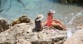 Young pretty women in swimsuit and coverup sitting on the rocks near the sea