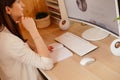 Young pretty working woman with long dark hair sitting at desk with notebook, white keyboard, mouse, column speakers. Royalty Free Stock Photo