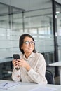 Young professional Asian business woman using phone looking away in office. Royalty Free Stock Photo