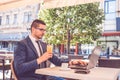 Young professional businessman wearing suit, drinking fresh orange juice and using  laptop outdoors Royalty Free Stock Photo