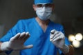 Young professional doctor in a blue medical uniform in rubber gloves in a white protective mask holds in his hand a metal scalpel
