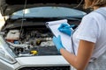 Young professional female mechanic inspects under the hood of a car.