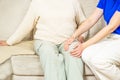 Young caregiver helping senior woman with knee pains at home. Caring nurse assisting her patient. Royalty Free Stock Photo