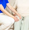 Young caregiver helping senior woman with knee pains at home. Caring nurse assisting her patient. Royalty Free Stock Photo