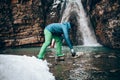 Young professional male tourist collects water from a mountain river.in winter.