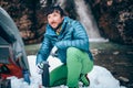 Young professional male tourist is drinking in the mountains near the river in winter.