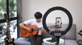 Young man playing guitar and streaming online vlog with smart phone.