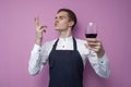 Professional sommelier in uniform holds a glass of red wine and enjoy the taste on a pink background, the guy the waiter tastes Royalty Free Stock Photo