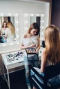 Young professional visagiste holding palette applying eyeshadow to the Caucasian female model in beauty shop