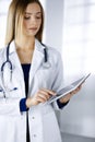 Young professional woman-doctor is using a tablet computer, while standing in a clinic. Portrait of beautiful female Royalty Free Stock Photo