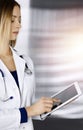 Young professional woman-doctor is using a tablet computer, while standing in a clinic. Portrait of beautiful female Royalty Free Stock Photo