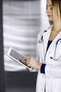Young professional woman-doctor is using a tablet computer, while standing in a clinic. Portrait of beautiful female Royalty Free Stock Photo