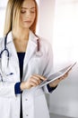 Young professional woman-doctor is using a tablet computer, while standing in a sunny clinic. Portrait of beautiful Royalty Free Stock Photo