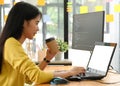 Young professional woman uses a laptop for work and online meetings, she holds a coffee cup and works from home