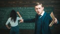 Young professor pointing at the board while holding book in straight hand. Young teacher giving explanations to students