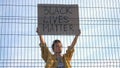 Young protesting woman standing behind the fence holds a poster - Black Lives Matter