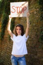 Young protesting woman in white shirt and jeans holds protest sign broadsheet placard with slogan `Stop` for public