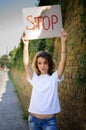 Young protesting woman in white shirt and jeans holds protest sign broadsheet placard with slogan `Stop` for public