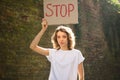 Young protesting woman in white shirt and jeans holds protest sign broadsheet placard with slogan `Stop` for public