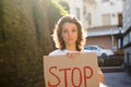 Young protesting woman in white shirt and jeans holds protest sign broadsheet placard with slogan 'Stop' for public