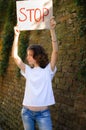 Young protesting woman in white shirt and jeans holds protest sign broadsheet placard with slogan `Stop` for public