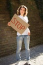 Young protesting woman in white shirt and jeans holds protest sign broadsheet placard with slogan `Stop` for public demonstratio