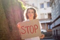 Young protesting woman in white shirt and jeans holds protest sign broadsheet placard with slogan 'Stop' for public