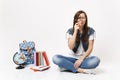 Young puzzled interested woman student holding looking on magnifying glass sitting near globe, backpack, school books Royalty Free Stock Photo