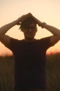 Young puzzled man in glasses with dreadlocks holding book above head as roof, standing in nature on sunset. Concept of Royalty Free Stock Photo