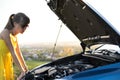 Young puzzled woman driver standing near her car with popped up hood looking at broken engine Royalty Free Stock Photo