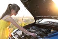 Young puzzled woman driver standing near her car with popped up hood looking at broken engine Royalty Free Stock Photo