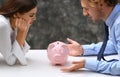 Young quarreling couple with piggy bank at table Royalty Free Stock Photo