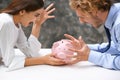 Young quarreling couple with piggy bank at table Royalty Free Stock Photo