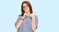 Young read head woman wearing casual clothes and glasses asking to be quiet with finger on lips pointing with hand to the side Royalty Free Stock Photo