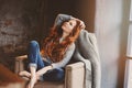 Young readhead woman relaxing at home in cozy chair, dressed in casual sweater and jeans